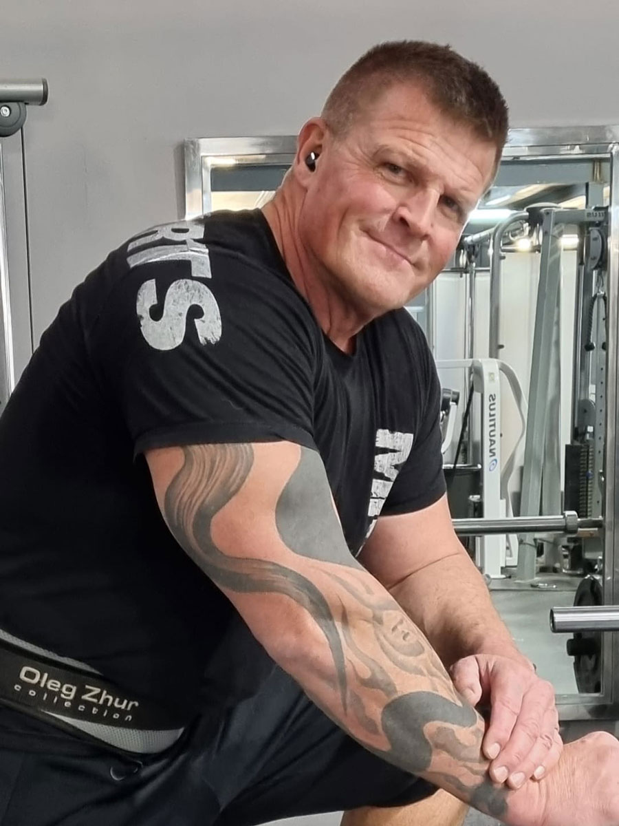 Træneren er i gymnastiksalen og smiler til kameraet.